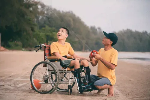NDIS participant in wheelchair enjoying beach kite-flying activity with support person, demonstrating community access