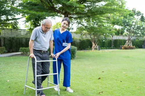 A caregiver assisting an elderly man with a walker in a peaceful outdoor setting, NDIS STA provided Melbourne